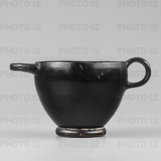 Black-finished skyphos, Greek ceramics, Type B. Thin-walled skyphos with a deep bowl and annular foot. One handle mounted horizontally, the other vertically. Entirely covered with a high-quality, glossy black varnish; only the bottom remains clay-colored with decoration of concentric circles. Technology: visible traces of turning; small chips on the surface. Clay color 2.5 YR 5/6 red. Varnish color 10 YR 2/1 black. Attributed to Attica, 480–450 BC. Vessel skyphos. Height 7.6 cm; width 14.1 cm; depth 8.8 cm; weight 0.102 kg., A black ceramic cup with a rounded body and a small pedestal base sits against a neutral gray background, showing a simple loop handle on one side and a short spout-like extension on the opposite side; the cup's surface is mostly smooth with a few small scuffs and lighter spots, and there are subtle variations of black and dark brown on the rim and base.