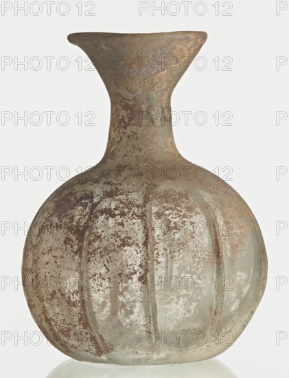 Flask; body in the shape of a flattened sphere, decorated with ribs;, Syria, 2nd–3rd century AD. Transparent, colourless, iridescent glass. Slightly flattened spherical body decorated with vertical thin, uneven ribs; short cylindrical neck terminating in a funnel-shaped spout with a thickened and rounded edge; free-blown. Outer diameter of the spout: 3.80 cm. Height: 8.80 cm. Body diameter: 8 cm. Bottom diameter: 3.40 cm. Type: Isings form 101? Weight: 0.030 kg., A round, bulbous glass vessel with a narrow neck that flares outward at the rim, showing a textured, weathered surface with speckled and patchy areas; the glass appears translucent with a patina of earthy brown and rusty tones over pale greenish and clear glass, and there are a few vertical rib-like grooves around the body.
