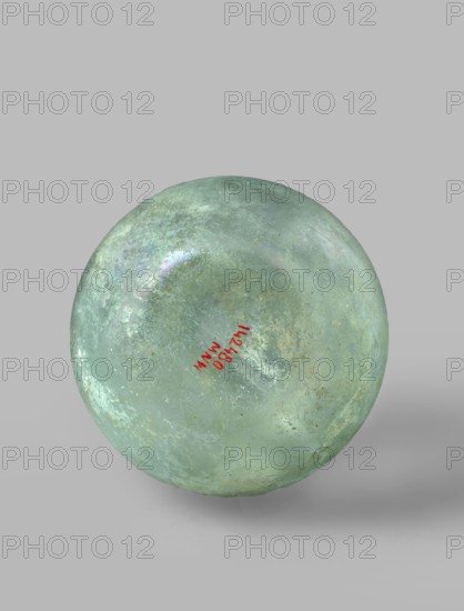 Flask with a spherical body and a high, cylindrical neck ending in a wide, straight-cut rim. The neck is marked by a recess and is decorated with a ring under the rim. Concave bottom with rounded edges. The neck is set obliquely to the body. Translucent, green glass. Spherical body, cylindrical neck slightly flaring upwards, straight rim with rounded edge, heat-worked. Neck narrowed at the bottom; free blowing. Type: Isings form 104B, 3rd–4th century, Phoenicia; vessel. Dimensions: height 18.4 cm; width 13.2 cm; rim diameter 4.9 cm; foot diameter 6 cm; maximum diameter 11.9 cm., A spherical object with a weathered, mottled surface in shades of green and aqua with areas of pale turquoise and faint mottlings of whitish and grey; the sphere has a slightly iridescent sheen in places and small spots of darker green and brownish discoloration; it sits against a smooth light grey background and casts a soft shadow beneath it.
