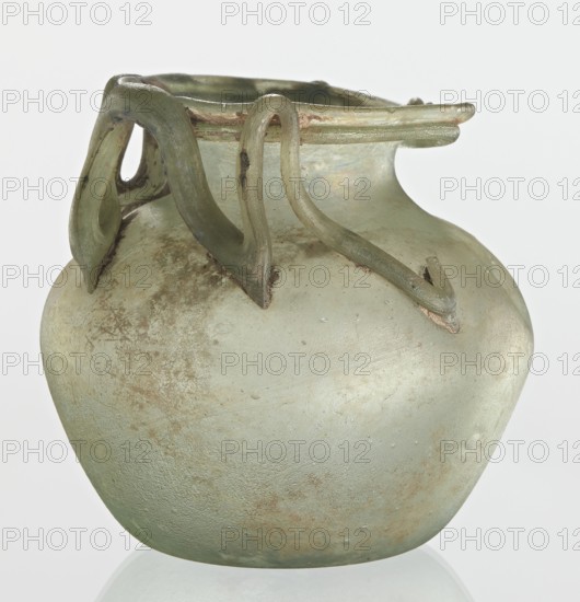 Bottle, unknown eastern workshop, Goluchów Greater Poland Voivodeship, 3rd century, vessel, height 7 cm, width 8.5 cm, A rounded glass vessel with a bulbous body and a short neck, showing a pale green and translucent surface with areas of iridescence and brownish weathering, topped by several applied ribbon-like glass handles or decorative loops in a darker green, with the rim slightly flared and the base resting on a reflective light surface; overall colors visible include pale green, darker green, brown, and hints of iridescent rainbow sheen.