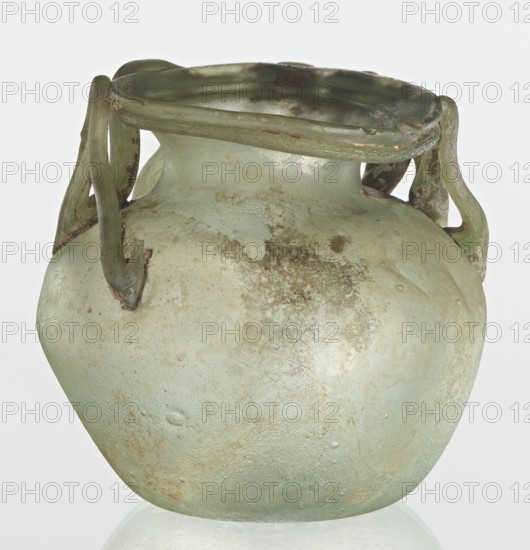 Bottle, unknown eastern workshop, Goluchów Greater Poland Voivodeship, 3rd century, vessel, height 7 cm, width 8.5 cm, A translucent pale green glass vessel with an ovoid body and a short neck topped by a flattened rim, showing a slightly iridescent sheen and areas of brownish discoloration and weathering; a group of looped handles attach near the rim and shoulder, also in pale green with darker green and brown patches; the surface displays cloudy textures, small bubbles, and roughened worn spots; the background is a light neutral tone.