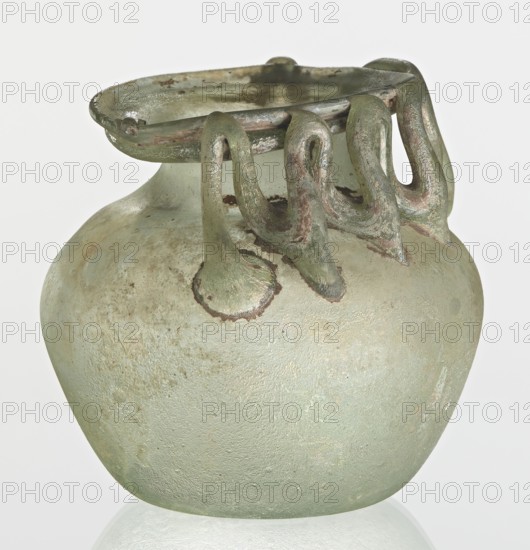 Bottle, unknown eastern workshop, Goluchów Greater Poland Voivodeship, 3rd century, vessel, height 7 cm, width 8.5 cm, A rounded glass vessel with a wide flaring rim and decorative looped applied handles around the neck. The surface shows a weathered, slightly rough texture with irregular patches and residues. The vessel and its applied elements are predominantly pale green with areas of lighter and darker green, some muted brownish and grayish tones on the loops and rim, and a few dull iridescent sheens. The background is plain and light.