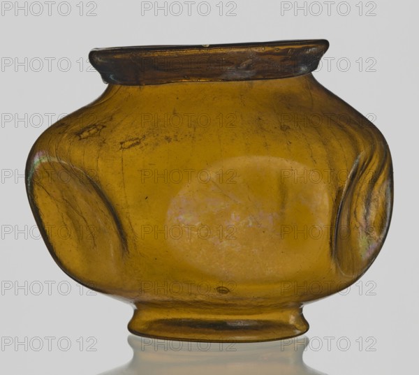 Vessel, Goluchów Greater Poland Voivodeship, vessel, height 10.2 cm, width 13.2 cm, A rounded glass vessel with a short flared neck and a small foot, shown against a pale background; the glass is amber with areas of darker brown near the rim and subtle iridescent sheens in places, with surface imperfections, slight scratches, and a few cloudy patches visible within the body.
