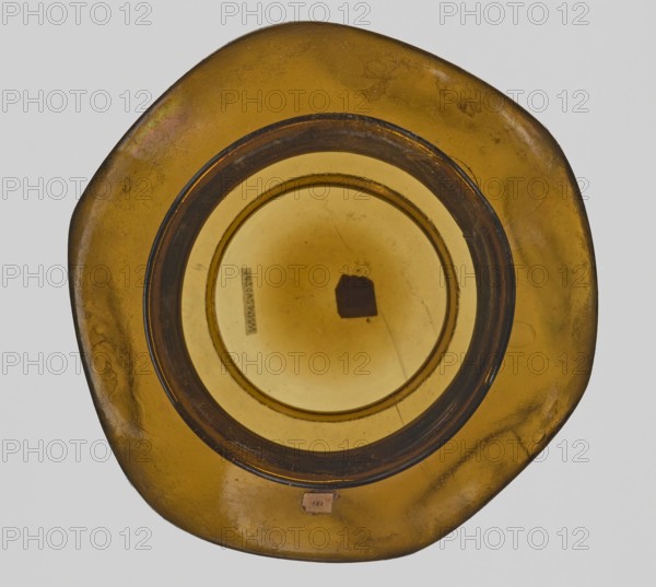 Vessel, Goluchów Greater Poland Voivodeship — place of origin, vessel, height 10.2 cm, width 13.2 cm, A top-down view of a circular glass object with an irregular outer rim, primarily amber and golden brown in color, with a darker brown ring near the center and lighter amber tones toward the middle; the glass surface shows a few small blemishes, spots, and tiny scratches, and there is a small darker irregular shape inside the central area.