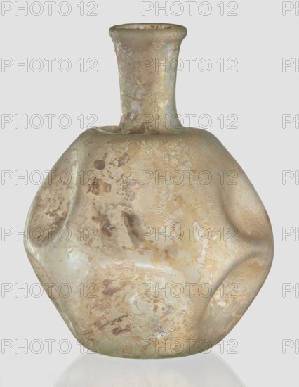 Flask, unknown eastern workshop, 3rd–4th century AD, vessel, height 11 cm, A glass vessel with an irregular, flattened form and a short neck topped by a flared rim; the surface shows a weathered, iridescent appearance with a mottled pattern in shades of beige, tan, brown, cream, and pale green, with subtle areas of pearly sheen and occasional darker brown patches.