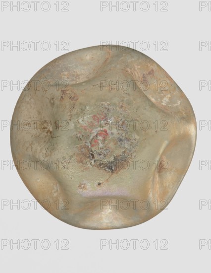 Flask, unknown eastern workshop, 3rd–4th century AD, vessel, height 11 cm, A rounded, irregularly shaped object with a lumpy, dented surface showing a mix of muted greens, pale beige, tan, and sandy browns, with areas of darker brown and rusty orange mottling. The surface has patches of rough, pitted texture and smoother, slightly glossy areas, with a central region that contains a mix of speckled discoloration in gray, brown, and dull red, and subtle iridescent sheen in places. The background is a uniform light gray.