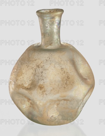 Flask, unknown eastern workshop, 3rd–4th century AD, vessel, height 11 cm, A rounded, irregular glass vessel with a narrow neck and slightly flared rim sits against a pale gray background; the glass surface shows a weathered, pitted texture with iridescent sheens and matte areas in muted colors including beige, pale gold, sandy brown, pearly white, faint green, and hints of pastel purple, with mottled patches and subtle streaks across its bulbous body and neck.