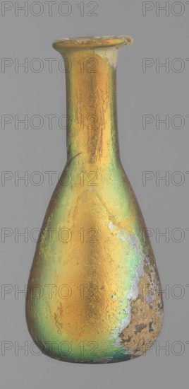 Flask, unknown eastern workshop, Goluchów Greater Poland Voivodeship, glass, antiquity, Roman Empire. Flask with a slender, pear-shaped body and a lower neck ending in a ring-shaped rim. Flat bottom. Covered with multicolored patina. 1st–2nd century, vessel, height 9.4 cm, A narrow-necked bottle with a flared rim, shown against a plain gray background, displaying an iridescent surface with dominant gold and green tones and areas of worn or rough texture in muted gray and brown.