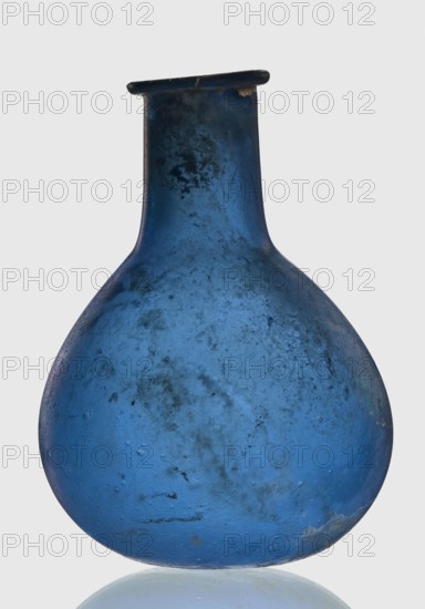 Bottle, unknown eastern workshop, 1st–2nd century, vessel, height 7.5 cm, width 5.5 cm, A single bulbous glass vessel with a narrow neck and a flattened rim, shown against a plain light background; the glass is predominantly deep blue with areas of darker blue and muted blackish speckling and clouded patches, and there are subtle lighter blue highlights and a few pale cloudy spots on the surface.
