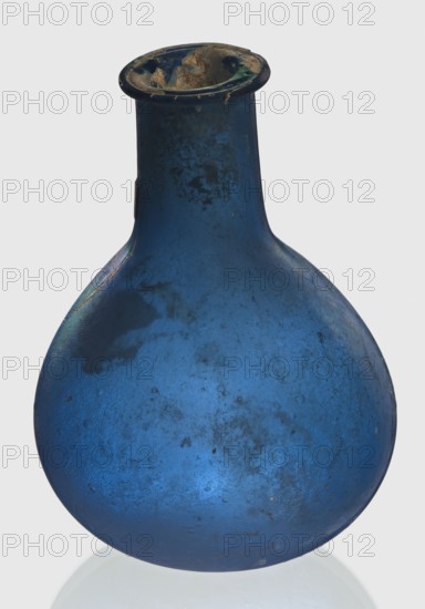 Bottle, unknown eastern workshop, Goluchów Greater Poland Voivodeship, 1st–2nd century, vessel, height 7.5 cm, width 5.5 cm, A rounded glass vessel with a bulbous body and a narrow neck, shown against a pale background, predominantly deep blue with areas of darker mottling and lighter bluish highlights; the rim appears darker with patches of greenish and brownish discoloration and some rough, irregular deposits; the surface of the body shows a few cloudy, textured spots and subtle variations in blue tones, including hints of teal where light catches the curved form.