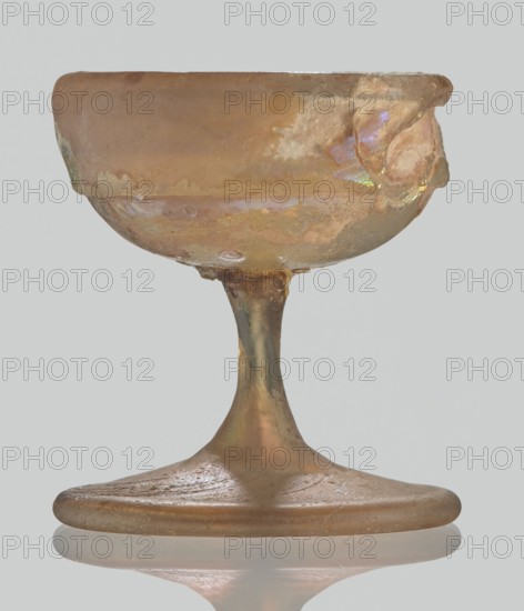 Cup, Egyptian workshop, Goluchów Greater Poland Voivodeship, 3rd–4th century AD, Roman Empire 27 BC–476, vessel, height 3.1 cm, width 3.2 cm, A small goblet-shaped object with a shallow rounded bowl on a tapered stem and a wide flattened base, showing an uneven, weathered surface and rough edges, with an iridescent sheen and patches of matte areas; colors visible include brown, tan, gold, pale green, and hints of purple and pink.