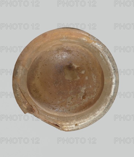 Cup, Egyptian workshop, Goluchów Greater Poland Voivodeship, 3rd–4th century AD, Roman Empire 27 BC–476, vessel, height 3.1 cm, width 3.2 cm, A round, shallow bowl viewed from above with a worn, uneven rim and a small broken section; the surface shows mottled textures and spots, with a central smoother depression and scattered pitting; colors visible include shades of brown, tan, beige, with hints of pale gray and faint metallic sheen along parts of the rim; the background is a flat light gray.