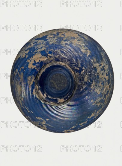Bottle, unknown eastern workshop, Goluchów Greater Poland Voivodeship, 3rd–4th century, vessel, height 10 cm, width 3.8 cm, A round, bowl-shaped object viewed from above with a central circular opening and a concave interior, showing a worn surface with flaking and irregular patches; the visible colors include deep blue, lighter blue, beige, gray, and hints of iridescent purple and green, with concentric ripple-like rings around the central opening and a mottled, weathered texture across the surface.