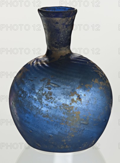 Bottle, unknown eastern workshop, Goluchów Greater Poland Voivodeship, 3rd–4th century, vessel, height 10 cm, width 3.8 cm, A rounded glass vessel with a narrow neck and flared rim, showing a mottled surface in shades of deep blue and lighter blue with patches of dull gold and brown discoloration; the neck appears darker with similar gold-brown mottling, and the body displays a few shallow indentations and irregular textured marks across its surface, all set against a pale neutral background.