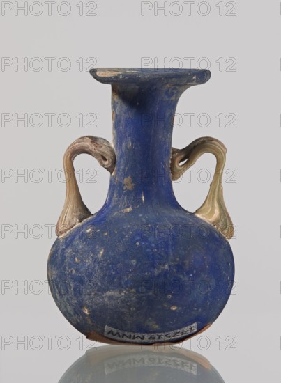 Amphora, bulging belly with a rounded bottom, long cylindrical neck with a thick ring-shaped rim; handles attached to the shoulders and halfway up the neck. 3rd–4th century, Roman Empire 27 BC–476. Vessel. Height 4.7 cm, width 3 cm., A small rounded vessel with a tall narrow neck and a flared rim, predominantly deep blue in color with patches of lighter blue and white speckling, featuring a pair of curved handles that are beige and pale green with some brownish tones, resting on a reflective surface that mirrors the bottom of the vessel; the rim shows worn areas revealing a lighter, claylike color and the body has spots of surface wear and small pitted marks.