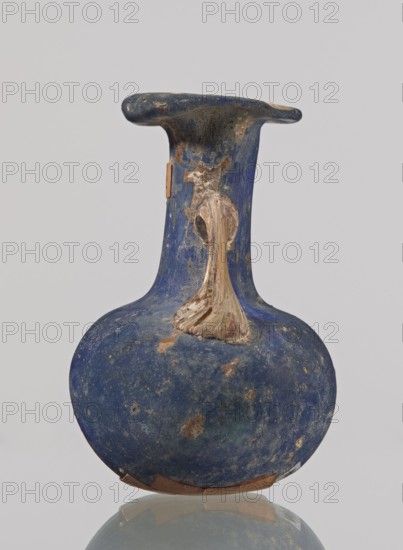 Amphora, bulging belly with a rounded bottom, long cylindrical neck with a thick ring-shaped rim; handles attached to the shoulders and halfway up the neck, 3rd–4th century, Roman Empire 27 BC–476, ceramic vessel, height 4.7 cm, width 3 cm, A single rounded vessel with a narrow flaring neck and a wide flat rim is shown against a plain light background; the vessel has a worn, textured surface in deep blue with areas of lighter blue and greenish patina and patches of brown and beige where the surface has flaked away; a raised handle-like feature in a beige to tan color extends from the neck onto the shoulder, showing layered, textured brushlike marks; the rim and neck show darker blue with scattered brown spots and small rough areas, and the base edge has fragments of brown material adhered, with the vessel resting on a reflective surface that creates a faint mirror image.