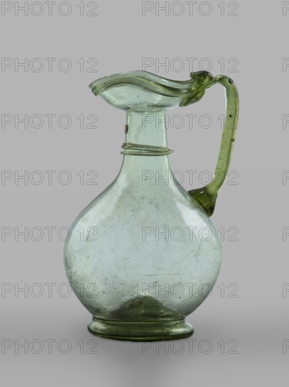 Oinochoe, Transparent, light green glass. Spherical belly on a foot with a clearance, created by pressing inward the central part of the bottom of the vessel; decoration on the cylindrical neck formed by a single glass thread of the same color, wound horizontally. The vice is glued to the arms and extends in an arc to the edge of the trefoil rim; free-blown. 4th century, Cyprus; vessel oinochoe. Base diameter 4.8 cm; weight 0.062 kg., A rounded glass pitcher with a bulbous body and a narrow neck topped by a flared, wavy rim, featuring a curved handle attached from rim to shoulder; the glass appears translucent with a pale green and slightly bluish tint, showing surface blemishes and small dark specks, and the background is a uniform gray.