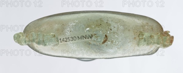 Ampoule, Egyptian workshop, 3rd century, Roman Empire 27 BC–476, glass vessel, height 12 cm, width 7.3 cm, An elongated, flattened glass vessel seen from the side with a translucent, pale green surface that shows areas of cloudiness and iridescent sheen, along with patches of brownish discoloration and small dark speckles; a pair of ornate, twisted handles of the same pale green glass project from opposite ends, showing similar weathered texture; the background is a uniform light gray.