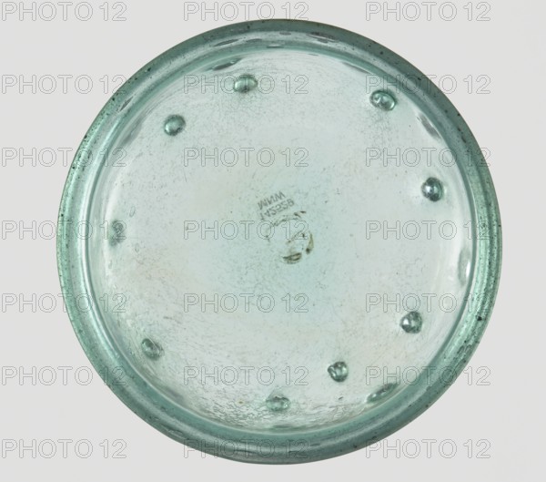 Bowl decorated with knobs. Hemispherical shape, decorated with pinched projections., 3rd–4th century AD. Type: Isings form 96b2. Translucent green glass with visible streaks in the glass mass; free-blown. Outer diameter of the rim: 9.30 cm. Height: 8.20 cm. Outer diameter of the bottom: 3.80 cm. Roman Empire 27 BC–476. Vessel; weight 0.134 kg., A round, shallow glass object viewed from above with a pale greenish-blue tint and a slightly darker green rim, showing a few small raised bumps around the interior surface and several faint, cloudy areas and scratches; the glass has a somewhat uneven, textured appearance with small bubbles and speckles visible, and the background is a light neutral color.