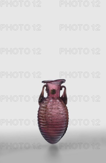 Amphora, unknown eastern workshop; De Tommaso form 20. Translucent manganese glass; elongated ovoid body covered with horizontal ribs and an outwardly flaring rim; body blown in a two-part form, neck and rim freely blown. Outer diameter of the rim: 3 cm; 2nd half of the 1st century. Vessel amphora. Weight 0.024 kg., A small ribbed glass vessel with a rounded, elongated body and a flared rim, featuring a pair of looped handles attached near the neck; the glass is translucent with shades of purple and pink, with darker purple accents and some brownish tones, and the surface shows textured horizontal ridges and small irregularities.