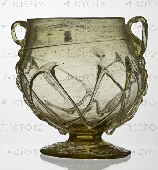 Skyphos, Deep bowl with wide foot and two small vertical handles. Surface decorated with a zigzag ornament applied with irregular threads. 3rd–4th century AD, Roman Empire 27 BC–476. Vessel; height 11 cm., A translucent greenish glass vessel with a rounded body and a flared rim, featuring a pair of looped handles on opposite sides and decorative raised trailing lines forming looping patterns around the body; the glass shows internal bubbles and small inclusions, subtle striations, and areas of slight cloudiness, and it rests on a flattened circular foot with textured surface; visible colors include pale green, yellowish-green, clear, and hints of darker green.