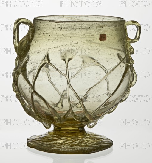 Skyphos, Deep bowl with wide foot and two small vertical handles. Surface decorated with a zigzag ornament applied with irregular threads. 3rd–4th century AD, Roman Empire 27 BC–476. Vessel, height 11 cm, A translucent pale green glass vessel with a rounded body on a flattened circular foot, featuring a few applied twisted glass handles on opposite sides and a group of thin raised glass trails decorating the exterior; the glass shows small interior bubbles and streaks and the surface has a slightly irregular, handcrafted appearance with green and yellowish tones.