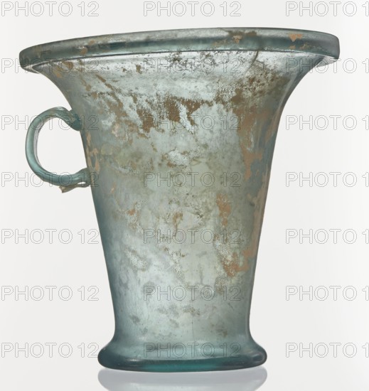Modiolus – drinking vessel, 1st century, Roman Empire 27 BC–476, from Goluchów Greater Poland Voivodeship; vessel, height 14.4 cm, width 15.4 cm, A large, flared vessel with a single loop handle on one side, showing a worn, mottled surface in shades of green, teal, pale blue, and brown with areas of lighter and darker patina; the rim is broad and slightly turned outward, the body tapers inward toward a rounded foot, and the handle attaches near the upper side; the surface displays irregular patches and streaks of discoloration and a slightly reflective, aged texture.