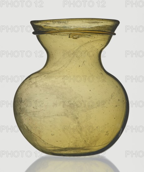 A viceless vessel, Goluchów Greater Poland Voivodeship, below the edge a glass thread is applied horizontally, unspecified place of origin, vessel, height 12.4 cm, width 10.7 cm, A translucent glass vessel with a bulbous body and a narrow neck flaring into a wide rim, shown against a pale background. The glass is an olive-yellow color with variations in tone and internal swirls and bubbles visible throughout. The rim has a slightly darker band around it and the surface shows small imperfections and streaks within the material. The base appears rounded and the vessel casts a faint reflection on the surface beneath it.