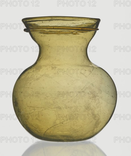 A viceless vessel, Goluchów Greater Poland Voivodeship, below the edge a glass thread is applied horizontally, unspecified place of origin, vessel, height 12.4 cm, width 10.7 cm, A translucent yellow-green glass vessel with a rounded body that narrows into a short neck and flares outward at the rim, showing a few surface imperfections and internal bubbles; a thin glass ring encircles the rim; the vessel sits on a reflective surface, and the background is a light neutral color.