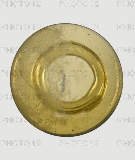 A viceless vessel, Goluchów Greater Poland Voivodeship, below the edge a glass thread is applied horizontally, unspecified place of origin, vessel, height 12.4 cm, width 10.7 cm, A round, translucent object with a yellowish color fills the frame, showing a glossy surface with a few small bubbles and imperfections trapped inside; the object has a shallow concave center and a raised rim, with areas of slightly darker and lighter yellow shading and some cloudy, textured patches on its surface against a pale, neutral background.