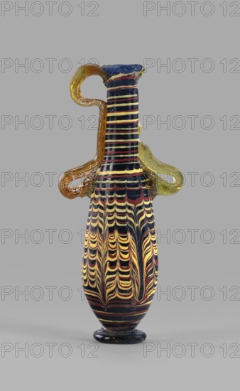 Amphoriskos; with an elongated neck; eastern Syrian or Cypriot workshop;, 2nd–1st century BC. Type: Grose group II:E, form III:4. Opaque glass, dark blue-green decoration in the form of festoon patterns made with yellow and brown threads; discoidal rim; neck widening slightly downwards; baggy belly; solid foot. Vertical vices one partially chipped, double vices made of translucent, light honey-green thread; formed on the core. Outer diameter of the rim: 2.25 cm. Height: 14.80 cm. Body diameter: 4.10 cm. Bottom diameter: 2.85 cm. Vessel; height 14.8 cm; width 4.1 cm., A tall slender glass vessel with a narrow neck and rounded base stands against a plain gray background; the body displays a repeating featherlike pattern in yellow and dark maroon on a black field, the neck has horizontal stripes in similar yellow and dark maroon on black, and the vessel has a small rounded black foot. A looped handle on one side is amber-colored with lighter speckling, and a second looped handle on the op...