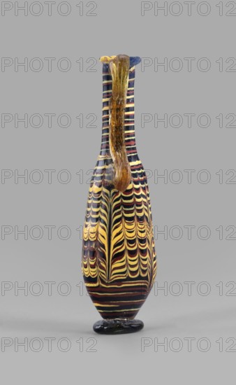 Amphoriskos; with an elongated neck; eastern Syrian or Cypriot workshop;, 2nd–1st century BC. Type: Grose group II:E, form III:4. Opaque glass with dark blue-green body and decoration of festoon patterns made with yellow and brown threads; discoidal rim; neck widening slightly downwards; baggy belly; solid foot. Vertical vices one partially chipped and double vices made of translucent light honey-green thread; formed on the core. Outer diameter of rim: 2.25 cm. Height: 14.80 cm. Body diameter: 4.10 cm. Bottom diameter: 2.85 cm. Vessel., A tall, narrow vase with a long neck and a curved handle standing on a rounded base, decorated with repeating wavy stripe patterns in yellow, black, and deep red, with the handle and parts of the neck showing a translucent amber-brown color and the top rim featuring a small area of blue; the background is a uniform light gray.