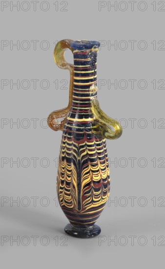 Amphoriskos; with an elongated neck; eastern Syrian or Cypriot workshop;, 2nd–1st century BC. Type: Grose group II:E, form III:4. Opaque glass with dark blue-green body and decoration of festoon patterns made with yellow and brown threads; discoidal rim; neck widening slightly downwards; baggy belly; solid foot. Vertical vices one partially chipped, double vices made of translucent light honey-green thread; formed on the core. Outer diameter of rim: 2.25 cm; height: 14.80 cm; body diameter: 4.10 cm; bottom diameter: 2.85 cm. Vessel., A slender glass vessel stands against a plain gray background, with a narrow neck, flared rim, and a rounded foot; the body displays a layered wavy pattern in black, yellow, and deep red that runs vertically and curves into scalloped motifs, while the neck features horizontal bands in the same colors. Two looped handles of translucent amber-yellow glass attach near the neck and shoulder, one forming a high loop and the other a lower hooked loop; the rim ap...