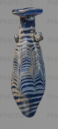 Alabastron with feathered decoration, Egyptian workshop, 6th–4th century BC, unknown place of origin; vessel alabastron, height 10.6 cm, width 3.7 cm, A narrow elongated glass vessel with a flared rim and a rounded pointed base, decorated with featherlike alternating bands creating a repetitive chevron pattern; the object shows areas of surface encrustation and weathering. The visible colors are deep blue, pale blue, white, and tan. The vessel has small rounded protrusions near the neck and a glossy glass surface with irregularities and worn spots.