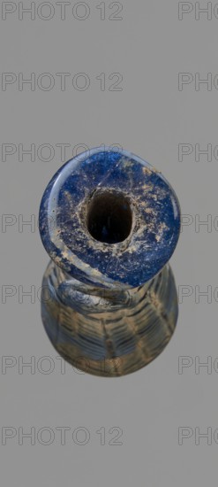 Alabastron with feathered decoration, Egyptian workshop, 6th–4th century BC, vessel; alabastron; height 10.6 cm, width 3.7 cm, A close-up vertical view of a rounded object with a central hollow, showing a textured surface in deep blue with patches of lighter blue and beige residue; the rim appears glossy and slightly worn, and the body below features a patterned surface with bands and ridges in muted blue and beige tones against a plain gray background.
