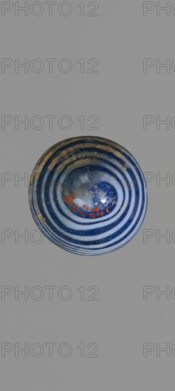 Alabastron with feathered decoration, Egyptian workshop, 6th–4th century BC, vessel; alabastron; height 10.6 cm, width 3.7 cm, A round object with concentric rings in shades of blue and white sits against a plain gray background; the object's surface shows areas of gold-toned wear and a few small orange-red marks, with a glossy finish and subtle reflections.