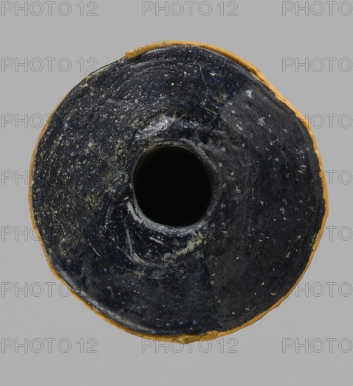 Alabastron, cylindrical belly, 4th–3rd century BC, vessel alabastron, height 17.4 cm, width 4.4 cm; maker and, A round object with a central hollow cavity, showing a predominantly dark surface with glossy black and deep blue areas speckled with lighter flecks, surrounded by a narrow band of yellowish ochre at the outer edge, set against a neutral gray background.