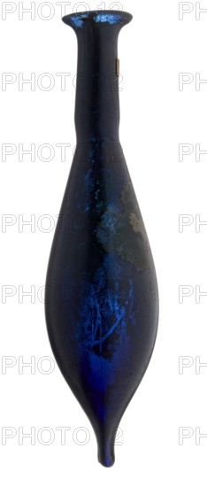 Vial, unknown eastern workshop, elongated belly with a pointed bottom, cylindrical neck and flared spout. Navy blue glass. 4th century, vessel, height 13 cm, width 1.8 cm, A tall, narrow vase-like object with an elongated teardrop shape and a flared rim, shown against a white background; its surface is predominantly dark blue to nearly black with areas of vivid metallic blue highlights and patches of lighter blue; there are a few irregular pale grayish or tan worn spots and mottling on one side; the form tapers to a rounded point at the bottom and has a smooth, slightly reflective texture overall.