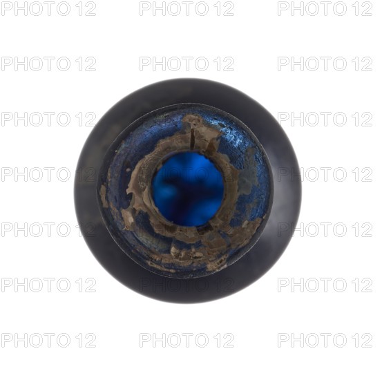 Vial, unknown eastern workshop, elongated belly with a pointed bottom, cylindrical neck and flared spout. Navy blue glass. 4th century, vessel, height 13 cm, width 1.8 cm, A top-down view of a round bottle opening showing a circular rim with peeling material and rough edges in shades of dark blue and brown, with a deep blue interior visible through the central opening; the outer body of the bottle appears dark, and the background is white.