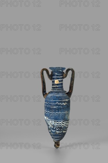 Amphorisko, Amphorisko with an ovoid belly, a long cylindrical neck ending in an uneven, slightly flaring rim, an uneven foot glued on, vertical, high, arched vises. Type: Grose III:E form III:2B, Harden form 7B. Opaque, dark blue glass decorated with white thread in a festoon pattern. The foot and vertical vises are made of dark amber, translucent glass; molding on the core. 2nd–1st century BC, Syria, vessel, amphorisko; rim diameter 2.8 cm; weight 0.110 kg., A narrow, elongated two-handled ceramic vessel sits upright against a plain gray background, the vessel predominantly deep blue with bands of lighter blue and white forming wavy and horizontal decorative patterns; the handles are dark brown to black with worn spots, and the rim and neck show similar deep blue tones with traces of lighter wear; the lower body tapers to a pointed, darker tip with some chipped areas revealing lighter material, and the surface has a slightly rough, aged texture.