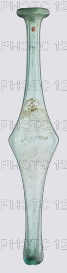 Unguentarium, unknown eastern workshop, Goluchów Greater Poland Voivodeship, with an elongated belly and a long neck, 3rd–4th century AD, unknown type of site/place of origin, vessel, height 36 cm, width 7 cm, A translucent elongated glass object with a narrow neck and flared ends, showing a pale greenish-blue tint throughout; the glass surface has cloudy areas, patches of discoloration, and a few small spots of darker residue, along with visible streaks and scratches; one end is slightly flattened and wider, the opposite end tapers and rounds, and the central section expands into a broader, diamond-like bulge with smoother curves; the background is a uniform light grayish color.