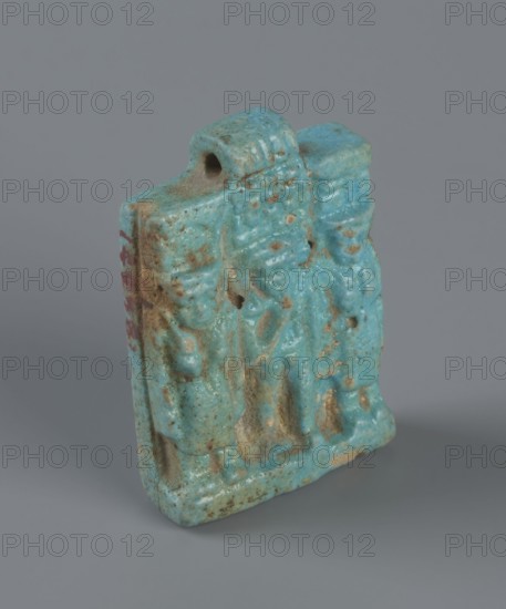 Amulet – plaque with a triad of deities: Harpocrates Horus, Isis, Nephthys. Amulet in the shape of a plaque with a triad of deities standing on a base. In the center is a figurine of Horus Harpocrates, on the left Isis, on the right Nephthys. The back of the plaque is flat. Pendant above the upper edge. Date: 664–30 BC, Late Period–Ptolemaic Period probably. Find country: Egypt. Object type: amulet. Dimensions: height 3.3 cm, width 2.2 cm, depth 0.7 cm., A small rectangular object with a rough, textured surface in shades of turquoise and aqua with areas of brownish and tan weathering, showing a raised, carved relief on its front and sides, an arched loop or hole near the top edge, and traces of darker reddish coloration along one side, set against a smooth grey background.