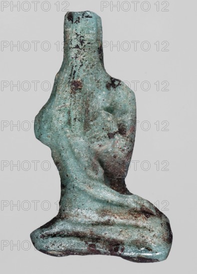 Amulet — seated goddess Isis; light blue glass; right hand raised to forehead, left hand lowered to knee; right profile; back smooth; Ptolemaic Period, 332–30 BC, Egypt; amulet; height 3.1 cm, width 2.7 cm., A rough, irregularly shaped object with a weathered surface, showing a dominant turquoise-green color with patches of darker green and black mottling, and areas of brownish rust and dirt; the form has a narrow, upright upper section that widens into a broader, rounded middle and base, with textured pitted surfaces and some smoother, eroded contours, giving an overall worn and corroded appearance against a light gray background.