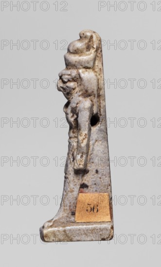Amulet - god Horus; creator, Horus mythology; double crown iconography, double crown on the head; Egyptian deities; 664–332 BC, Late Period, Egypt; amulet; height 3.8 cm, width 0.8 cm, A small carved figurine shown in profile against a neutral background, rendered in mottled off-white, beige, and brown tones with darker brown spots and weathered patches; the figure stands on a triangular base and wears a rounded headdress or crown, with a pronounced facial profile and a stylized beard or hair along the side; the torso and arms are visible in low relief with one arm along the body and a hole through the side of the piece; a small rectangular patch of tan material is attached near the base.