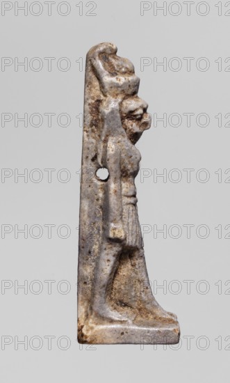 Amulet - god Horus; creator, Horus mythology; double crown iconography, double crown on the head; Egyptian deities; 664–332 BC, Late Period, Egypt; amulet; height 3.8 cm, width 0.8 cm, A narrow vertical carved figurine shown in profile, depicting a standing humanlike figure with a stylized head and pronounced facial features, wearing a short pleated garment and a headdress; the object has a rectangular backing with a round hole through it and a flat base. The surface shows a weathered, granular texture with patches of brown staining and areas of off-white and light gray tones, along with darker brown spots and some subtle beige areas.