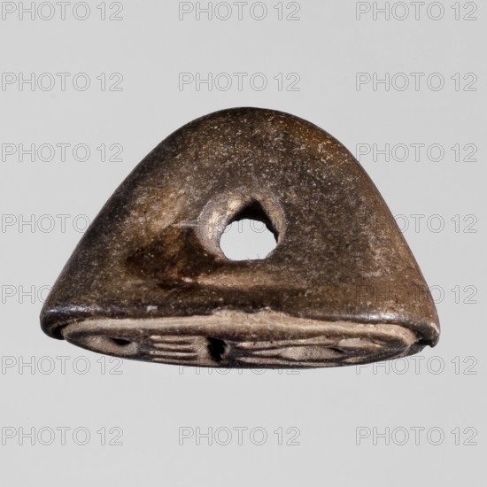 Amulet-seal with cartouche of Menkheperre Tuthmosis III, ca. 1479–1425 BC; convex handle; New Kingdom, Egypt, ca. 1550–1069 BC; seal/amulet; height 1.3 cm, width 2 cm., A small triangular object with a rounded top and a central hole, showing a worn, rough surface with visible texture; the object displays shades of brown, dark brown, tan, beige, and a little off-white along the lower edge, and it sits against a light gray background.