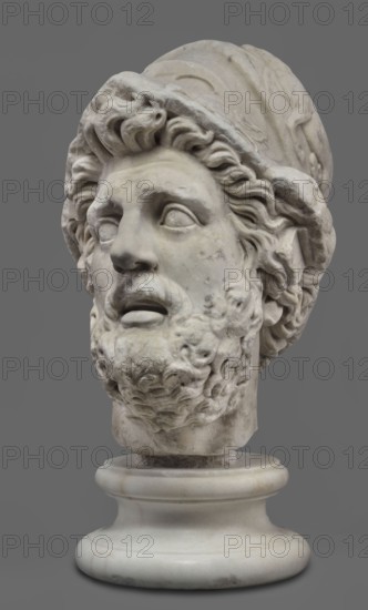 Head of Menelaus from the Menelaus Carrying the Body of Patroclus group, unknown artist. Head of a bearded man wearing a helmet, with an expressive face shown by wide-open eyes and parted mouth, emphasized by chiaroscuro effects from the contrast between lush locks of beard and hair emerging from under the helmet and the smooth skin of the face — the face of a man experiencing dramatic moments. The helmet is adorned with relief decoration depicting fantastic creatures: on each side a centaur fighting a Greek and, on the edge, a triton figurine. The sculpture is a Roman copy of the head from a Hellenistic bronze composition depicting Menelaus carrying the body of Patroclus. Menelaus, Helen's husband, is first to fight to retrieve the deceased's body and then carries it from the battlefield for burial; Patroclus's death is a pivotal moment in the Trojan War. Theme frequently reproduced in Roman sculpture. Dated broadly to the 1st half of the 2nd century AD reign of Hadrian, c. 117–138. R...