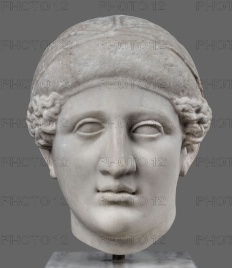 Head of Sappho Head of a Woman of the Kora Albani type, unknown Roman workshop; Sappho ca. 610–580 BCE, female portrait, Roman sculpture. Fragment of an ancient dowry or bust mounted on a modern bust. Numerous modern additions to details e.g., tip of the nose. The ancient part very good workmanship was originally part of a statue or bust herm?. Head slightly turned to the right, oval, idealised face. Hair covered with a headnet kekryphalos. The sculpture's original is identified as contemporary to Phidias, with dating supported by analogy to one of the Parthenon friezes. Type belongs to the Sappho/Kora Albani group, based on near-intact preservation. While the front is very well-crafted, the back is simplified and somewhat underdeveloped. This copy has several minor details altered compared to the original. Early 1st century, Roman Empire 27 BC–476, sculpture, weight 30.5 kg., A carved pale stone head of a person set against a gray background, showing a smooth rounded forehead and a cl...