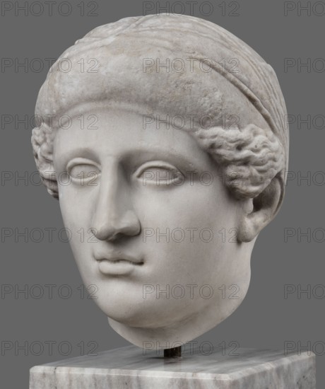 Head of Sappho Head of a Woman of the Kora Albani type, unknown Roman workshop; Sappho ca. 610–580 BCE, female portrait, Roman sculpture. Fragment of an ancient dowry or bust mounted on a modern bust. Numerous modern additions to details e.g., tip of the nose. The ancient part very good workmanship was originally part of a statue or bust herm?. Head slightly turned to the right, oval, idealised face. Hair covered with a headnet kekryphalos. The sculpture's original is identified as contemporary to Phidias, with dating supported by analogy to one of the Parthenon friezes. Type belongs to the Sappho/Kora Albani group, noted for near-intact preservation. Front is very well-crafted; back simplified and somewhat underdeveloped. Copy has several minor details altered compared to the original. Early 1st century, Roman Empire 27 BC–476, sculpture, weight 30.5 kg., A marble sculpture of a head displayed against a gray background, showing a smooth pale surface with subtle discoloration and weath...
