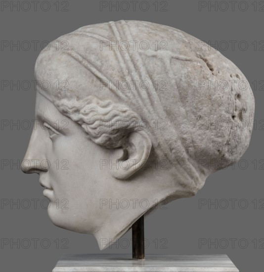 Head of Sappho Head of a Woman of the Kora Albani type, unknown Roman workshop, Scen. Gal. Klass., Sappho ca. 610–580 BC, female portraits, Roman sculpture. Fragment of an ancient dowry or bust mounted on a modern bust. Numerous modern additions to details e.g. tip of the nose. The ancient part very good workmanship was originally part of a statue or bust herm?. Head slightly turned to the right, oval, idealised face. Hair covered with a headnet kekryphalos. The sculpture's original is identified as contemporary to Phidias; dating is possible based on its analogy to one of the Parthenon friezes. Type belongs to the group known as Sappho/Kora Albani, based on the sculpture's near-intact preservation. While the front is very well-crafted, the back is simplified and somewhat underdeveloped. This copy also has several minor details altered compared to the original. Early 1st century, Roman Empire 27 BC–476, sculpture, weight 30.5 kg., A sculpted stone head in profile facing left, shown aga...